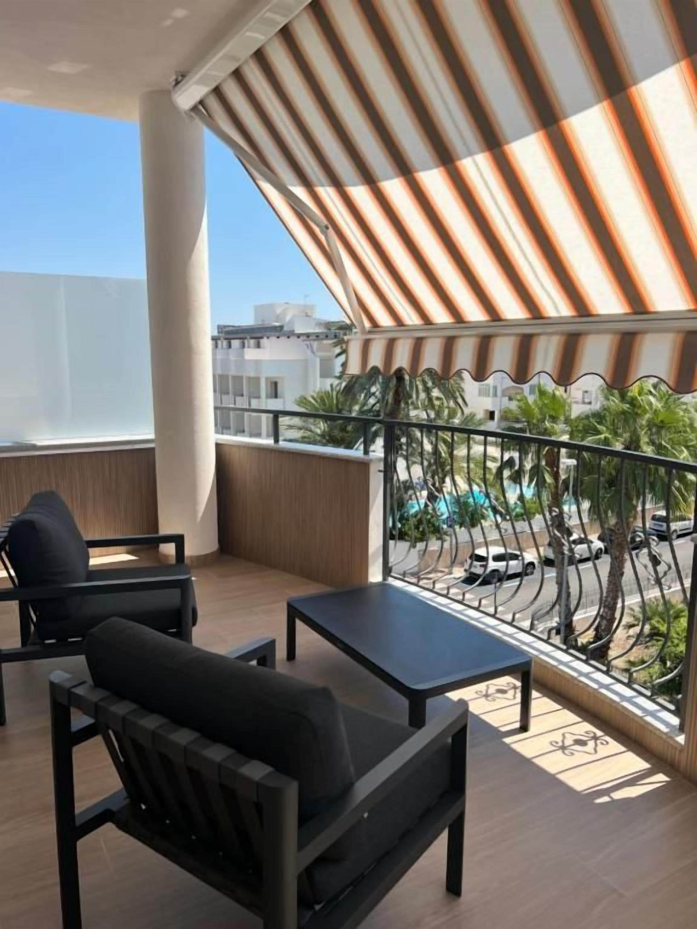 En balkon med markise, et bord og to stole, samt udsigt til gaden og bygninger.