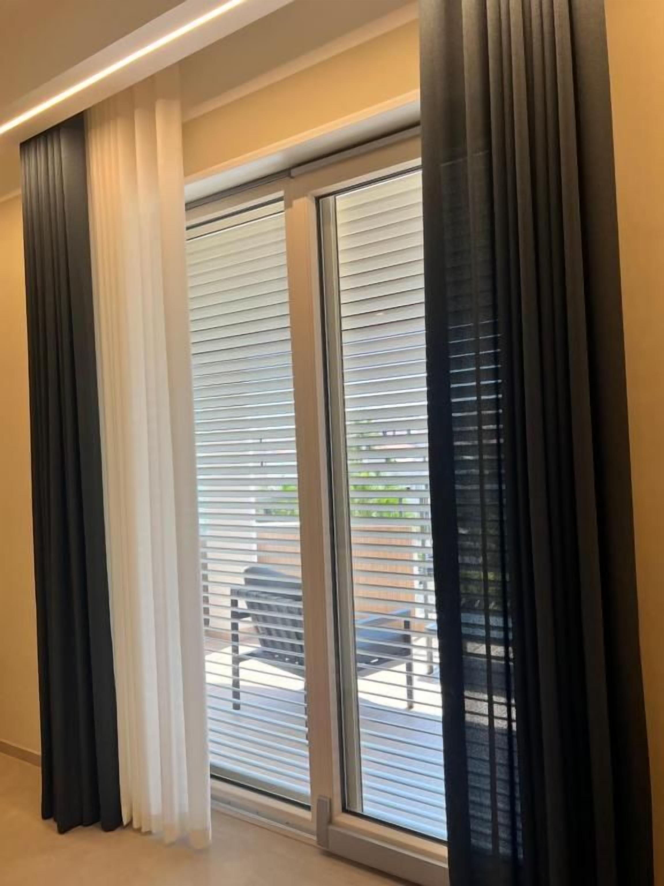 Una habitación con un amplio ventanal corredera que da a un espacio exterior, una lámpara en el techo y una ventana con persianas.