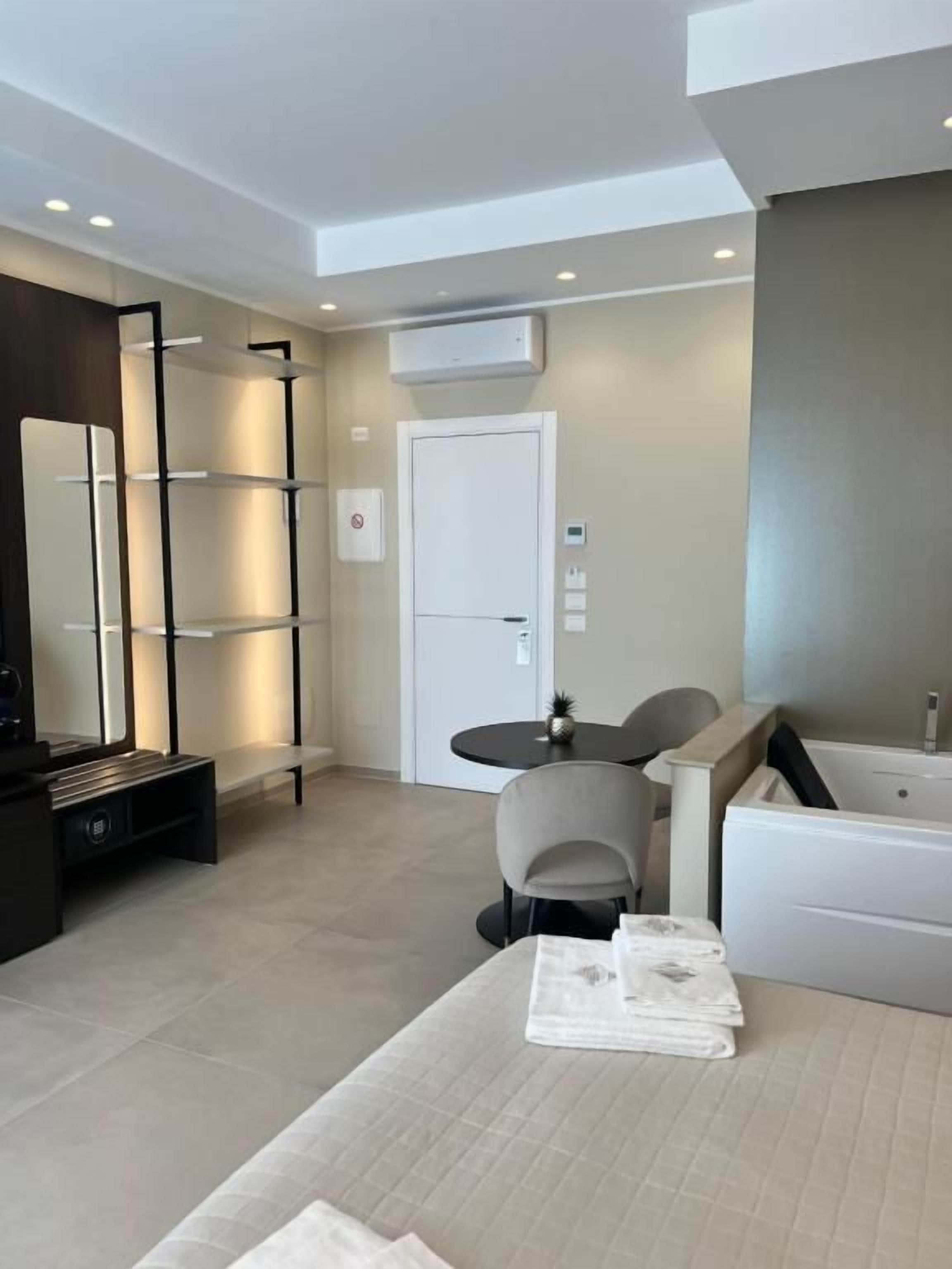 A modern hotel room with a bed, a small table, a chair, a desk, a shelf, a mirror, a door, and a bathtub.