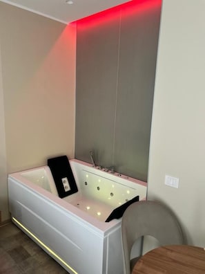 A modern bathroom with a large bathtub, a mirror, and a chair. - Manoli Luxury Rooms (Vieste)