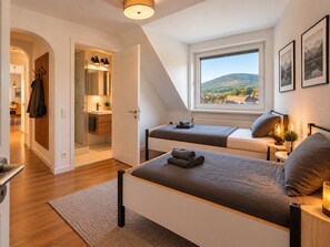 A bedroom with a large window, a bed, a bedside table with a lamp, and a view of a mountainous landscape. - Apartment 'Felix Living 16 – Lusenblick' for 2 guests (Mauth)