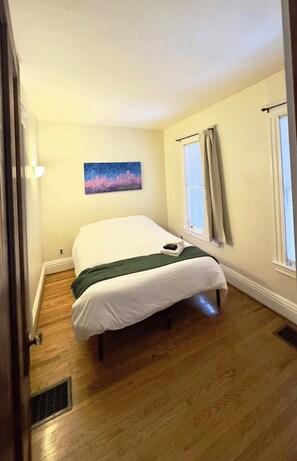 Quarto com cama, pintura, janela com cortinas e porta.