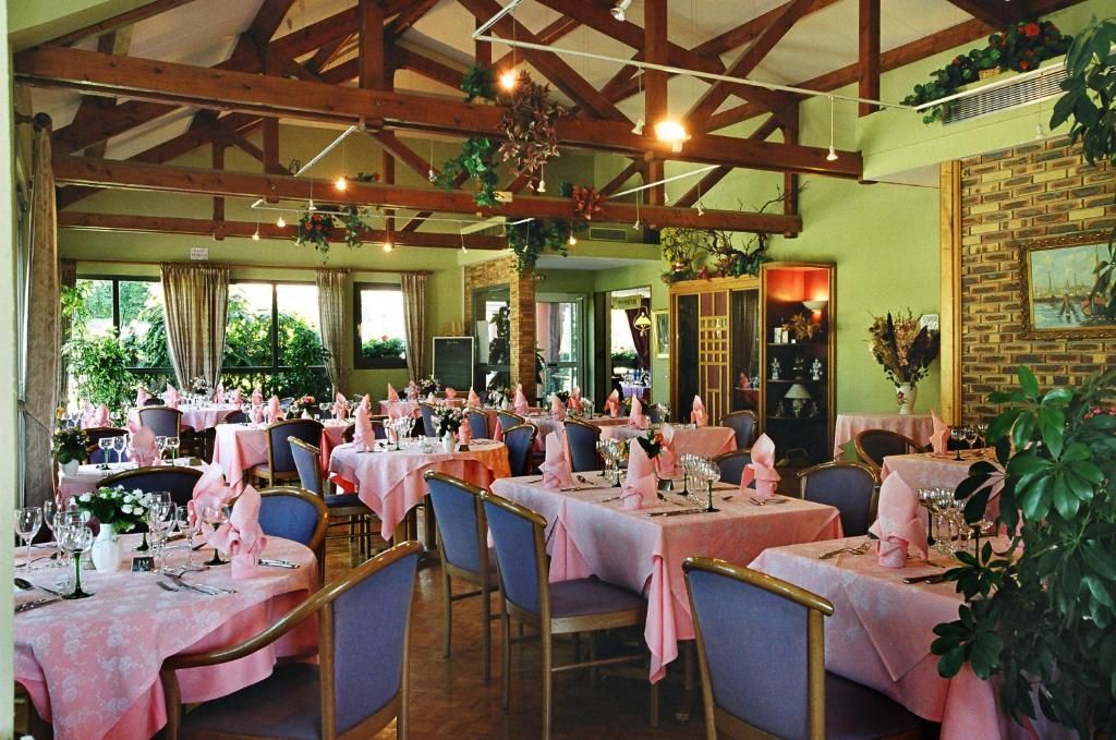 Ein Restaurant mit mehreren gedeckten Tischen, das durch eine rustikale Holzbalkendecke und grüne Wände gekennzeichnet ist.