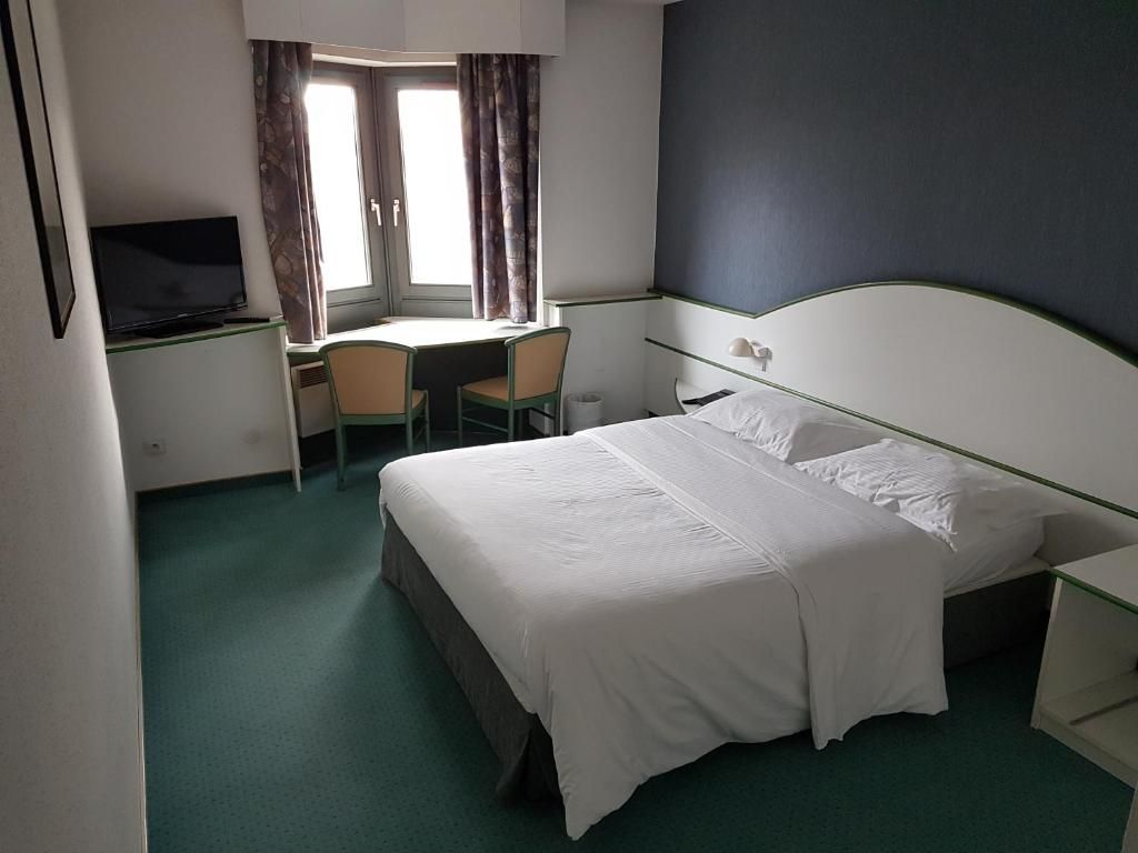 Une chambre d’hôtel équipée d’un lit, d’un bureau, d’une chaise, d’une télévision et d’une fenêtre avec des rideaux.