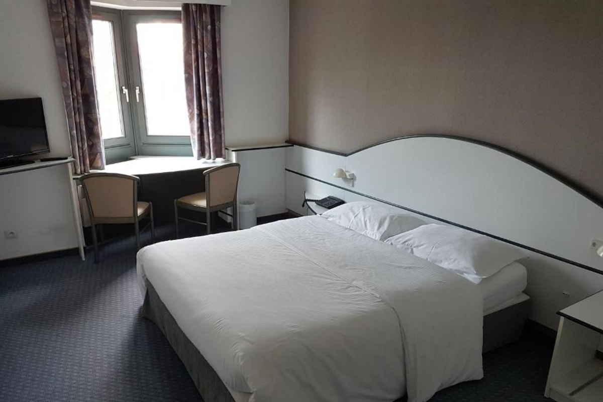 Una habitación de hotel con una cama, un escritorio, una silla y un televisor.