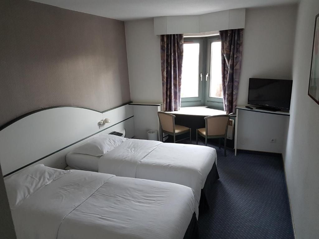 Ein Hotelzimmer mit zwei Betten, einem Schreibtisch, einem Fernseher und einem fenster mit Vorhängen.