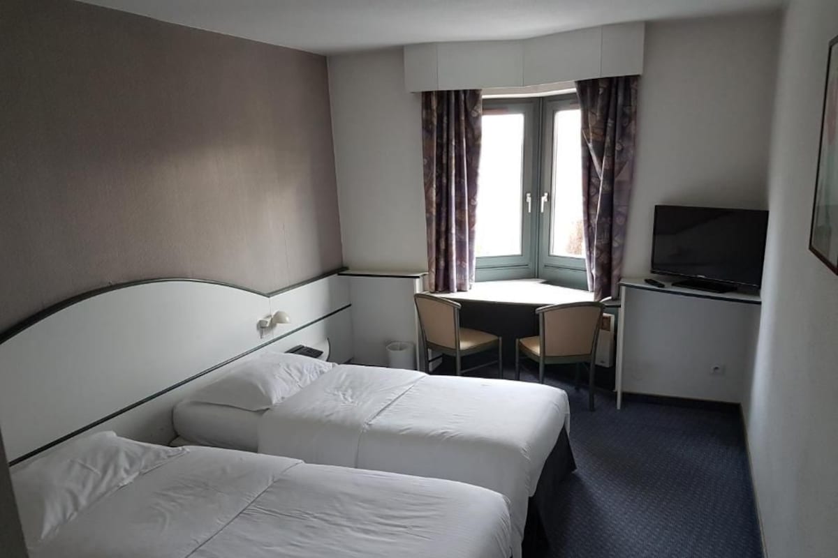 Habitación de hotel con dos camas, un escritorio, un televisor y una ventana con cortinas.