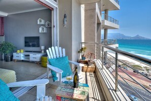 Un balcone con vista sull'oceano, un tavolo da pranzo con una bottiglia e una TV nella stanza.