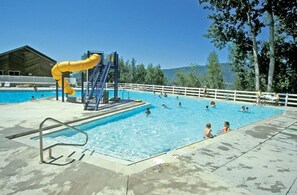 Une piscine avec un toboggan jaune, un plongeoir et une zone délimitée par une clôture.