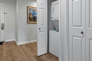 Una sala de bugaderia amb una rentadora i una assecadora blanques, una porta que condueix a una altra estada i un quadre penjat a la paret.