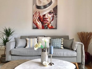 A living room with a grey sofa, decorative pillows, a vase with flowers, and a painting on the wall. - 1BDR Long Term Home/BASF/Parking/Netflix/Fast Wifi (Ludwigshafen am Rhein)