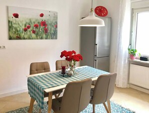 A dining area with a checkered tablecloth, chairs, a vase with red flowers, a hanging light fixture, and a refrigerator. - 1BDR Long Term Home/BASF/Parking/Netflix/Fast Wifi (Ludwigshafen am Rhein)