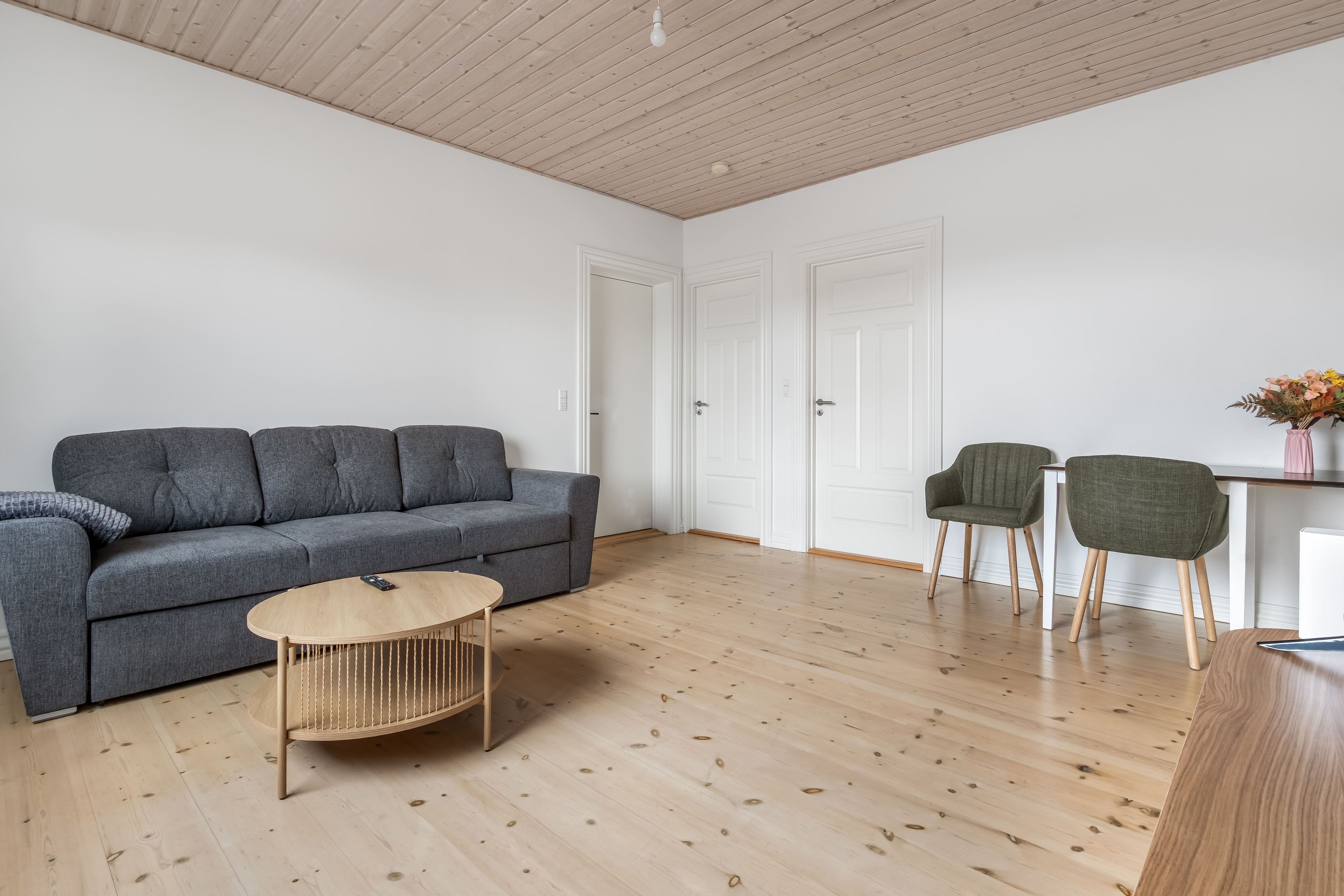 A modern living room with a grey sofa, a round coffee table, and two green chairs.