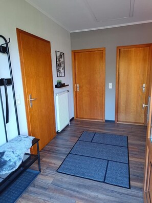 Un couloir avec trois portes en bois, un radiateur, un tapis noir et une petite étagère sur laquelle se trouve une plante.