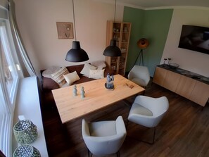 Un salon moderne avec une table à manger en bois, des chaises blanches, un canapé et un téléviseur.