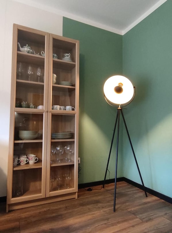 Une pièce avec un buffet en bois contenant de la verrerie et de la vaisselle, un lampadaire et un mur vert.
