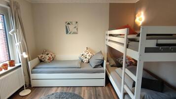 A room with a bunk bed, a sofa bed, a round rug, a radiator, and a window with curtains.