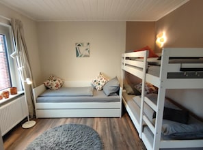 Une chambre avec un lit superposé, un canapé-lit, un tapis rond, un radiateur et une fenêtre avec des rideaux.