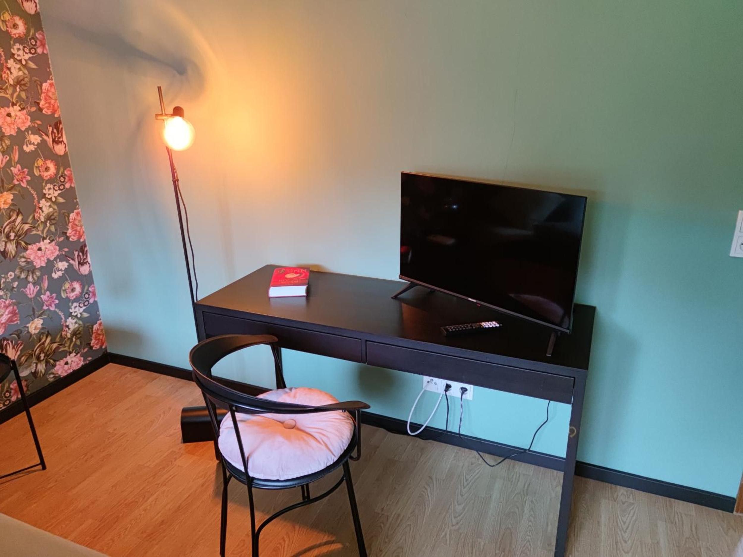 Ein Zimmer mit Schreibtisch, Stuhl, Fernseher und Lampe.