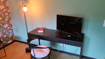 Ein Zimmer mit Schreibtisch, Stuhl, Fernseher und Lampe.