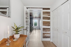 Un couloir avec un plancher en bois, une porte blanche et une plante posée sur une table en bois.