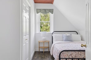 Ein Schlafzimmer mit einem Bett, einem Fenster, einer Lampe und einem kleinen Holztisch.