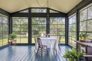A covered porch with a table and chairs, large windows, and potted plants. - The Halliday Creek Cabin (200 Acres of Privacy) (Greater Madawaska)