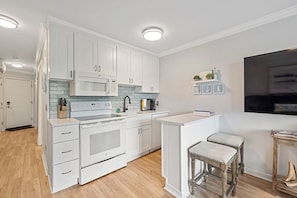 A modern kitchen with white cabinetry, a built-in microwave, and a central island with stools. - Coastal Charm – Ocean Views & Island Breezes! (HILTON HEAD ISLAND)