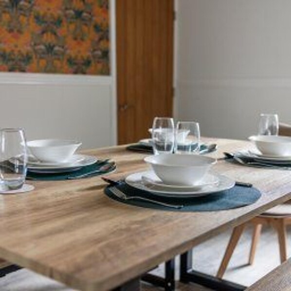 Una mesa de comedor con platos, tazones y vasos blancos, sobre una estructura de madera y patas metálicas.