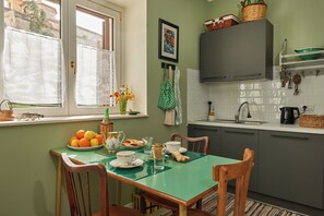 A kitchen with a dining table set for two, a window with curtains, and a green wall. - LACASETTA98 (Sperlinga)