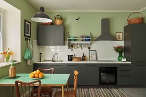 A modern kitchen with a green wall, white tiles, and a dining area with a table and chairs.