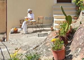 A person seated at a table with a chair, a basket, and a potted plant nearby. - LACASETTA98 (Sperlinga)