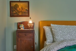 A bedroom with a bed, a nightstand with a lamp, a painting on the wall, and a wooden dresser.