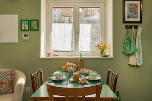 Un coin repas avec une table dressée pour deux personnes, une fenêtre avec des rideaux et une vue sur l’extérieur.