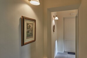 A hallway with a framed picture on the wall, a door at the end, and two wall-mounted lights.
