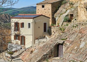 Un bâtiment en pierre avec un toit recouvert de tuiles rouges, un petit balcon doté de volets en bois et un escalier menant à une porte.