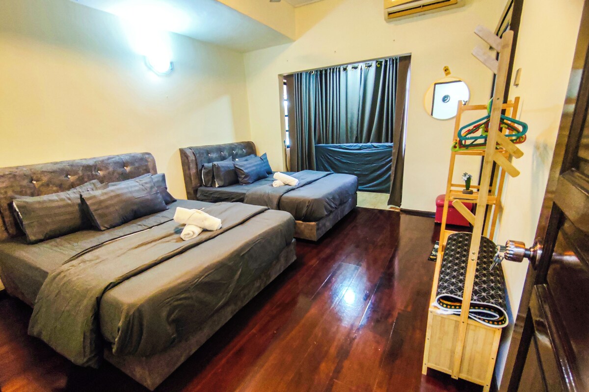 A hotel room with two beds, a wooden floor, a ceiling fan, and a window with curtains.