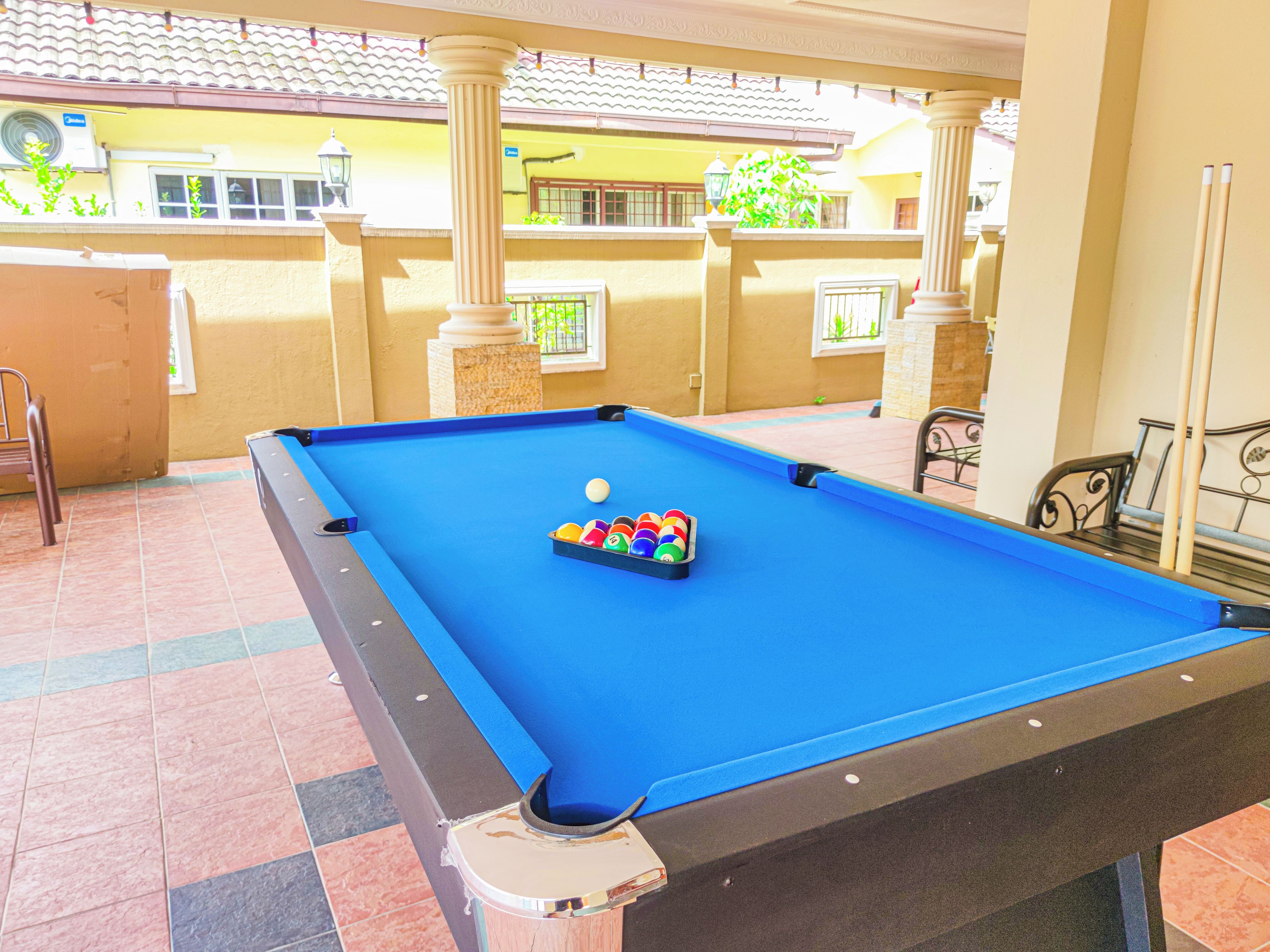 A pool table with a set of balls, a chair, and a table lamp in a room with tiled flooring and a balcony.