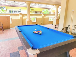 A pool table with a set of balls, a chair, and a table lamp in a room with tiled flooring and a balcony.