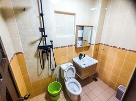 A bathroom with a toilet, sink, shower, and a green bucket.