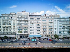 A multi-story building with balconies, a central entrance, and a street in front with cars and pedestrians. - Seafront Apartment | Panoramic Sea Views | Thessaloniki Center (Thessaloniki)