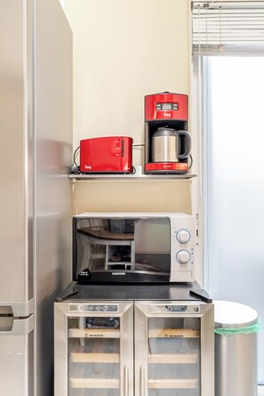 Une petite cuisine équipée comprenant un grille-pain rouge, une machine à café, un four à micro-ondes et deux réfrigérateurs.