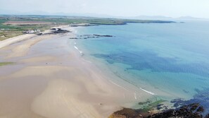 Eine Küstenlandschaft mit Sandstrand, klarem blauen Wasser und Bergen in der Ferne.