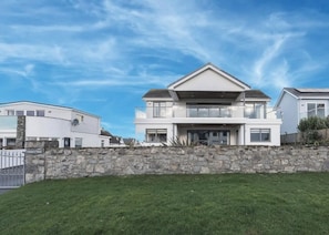 A two-story house with a stone wall in front, a clear sky, and a well-maintained lawn. - Luxury Family Beach House with Sea Views -Sleeps 8 - Pass the Keys (Rhosneigr)