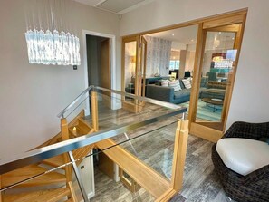 Een modern interieur met een trap met glazen balustrade, een rieten bank en een kroonluchter.