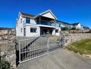 A two-story house with a gated entrance, a stone wall, and a clear blue sky. - Luxury Family Beach House with Sea Views -Sleeps 8 - Pass the Keys (Rhosneigr)