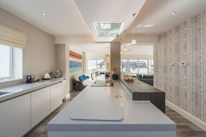 A modern kitchen with a central island, a dining area with a sofa, and a view through the window. - Luxury Family Beach House with Sea Views -Sleeps 8 - Pass the Keys (Rhosneigr)