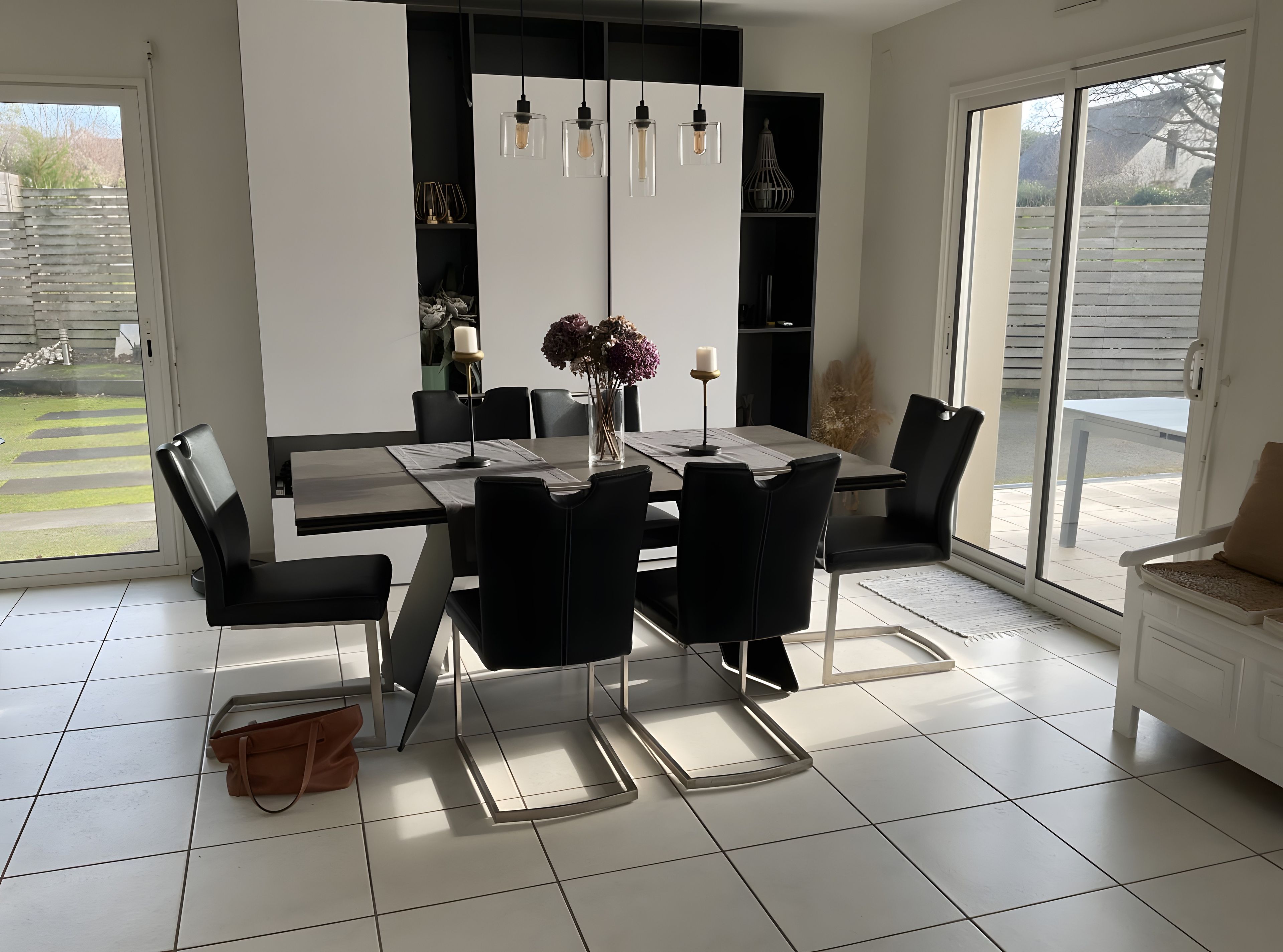 A modern dining area with a black and white color scheme, featuring a table set for four, black chairs, and pendant lighting.