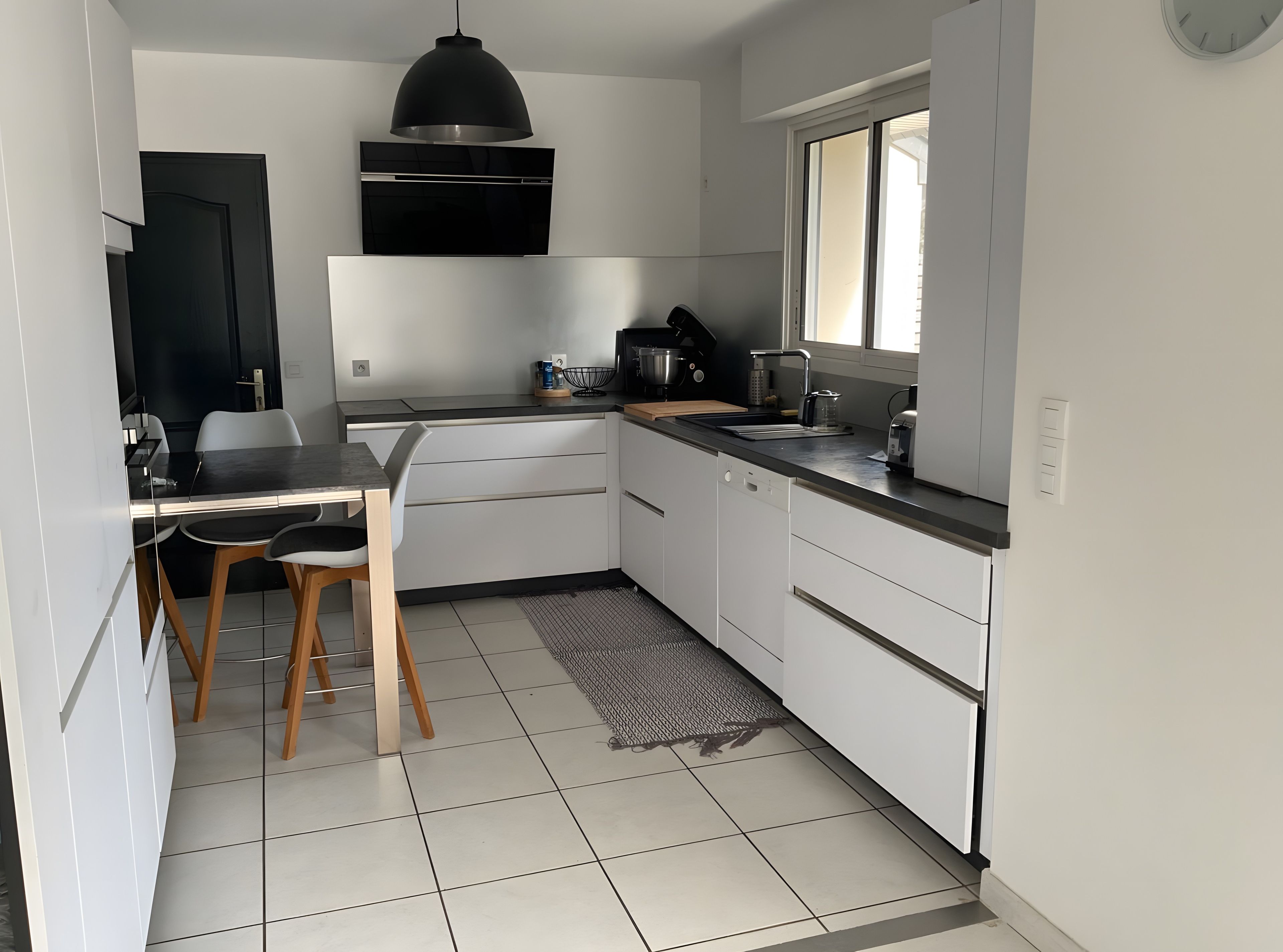 A modern kitchen with white cabinetry, a black countertop, and a window.