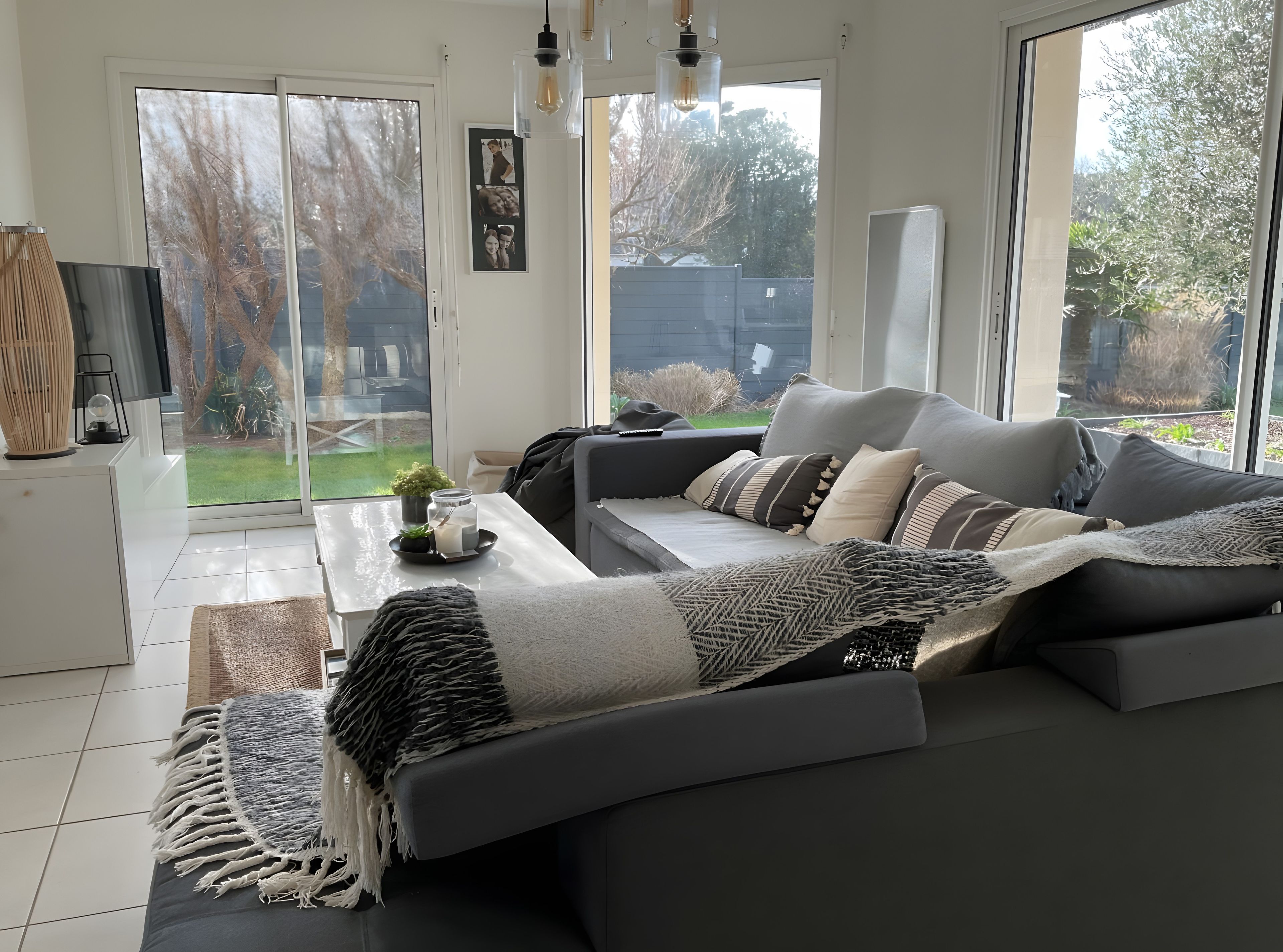 A modern living room with a grey sofa, a coffee table with decorative items, and a large window offering a view of the outdoors.